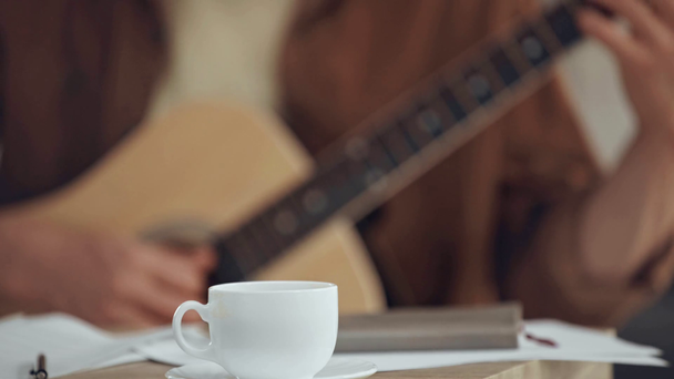 επιλεκτική εστίαση του ανθρώπου που παίζει ακουστική κιθάρα κοντά στο φλιτζάνι καφέ - Πλάνα, βίντεο