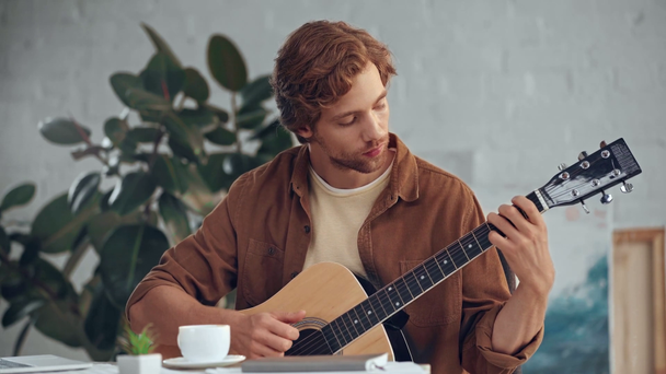 redhead man drinking coffee and playing acoustic guitar - Materiał filmowy, wideo