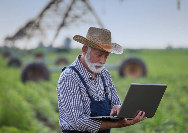 Farmer with laptop in front of irrigation system in field - Zdjęcie, obraz