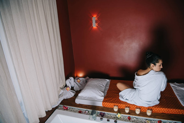 atractiva mujer en albornoz sentado en alfombra de masaje en el salón de spa
 - Foto, imagen