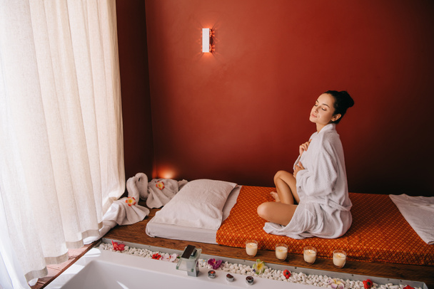 attractive woman with closed eyes in bathrobe sitting on massage mat - Photo, Image
