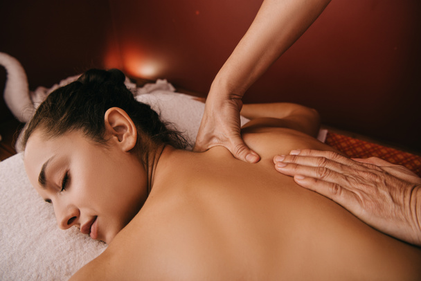 geschnittene Ansicht des Masseurs, der einer Frau auf einer Massagematte Rückenmassage gewährt - Foto, Bild