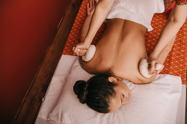 vue recadrée de masseur faisant massage du dos avec des boules à base de plantes à la femme dans le spa
 - Photo, image