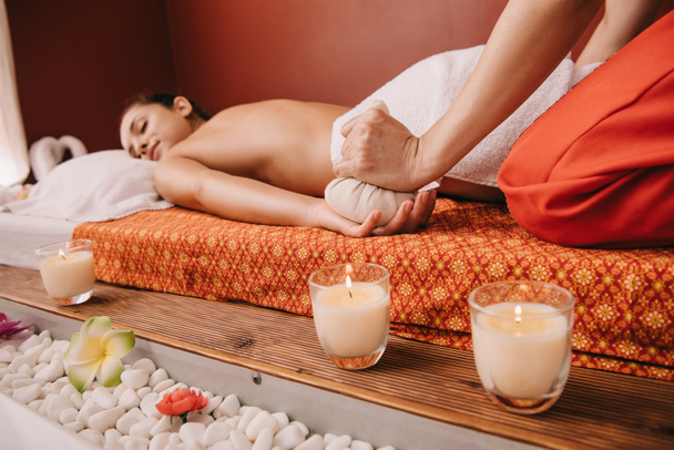 обрізаний вид масажиста робить масаж трав'яним м'ячем для жінки в спа-центрі
 - Фото, зображення