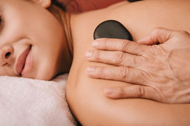 vue recadrée du masseur faisant massage aux pierres chaudes à la femme dans le salon de spa
  - Photo, image