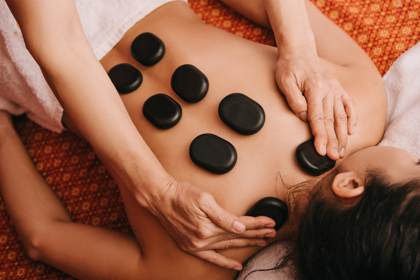 cropped view of masseur doing hot stone massage to woman in spa salon  - Photo, Image
