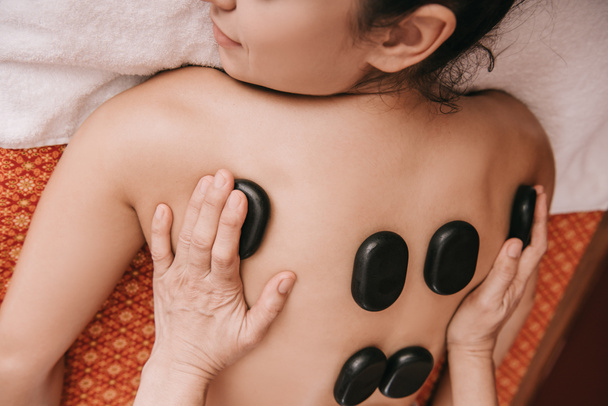 обрезанный вид массажера, делающего массаж горячими камнями женщине в спа-салоне
  - Фото, изображение