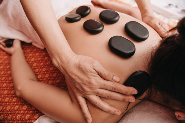 cropped view of masseur doing hot stone massage to woman in spa salon  - 写真・画像