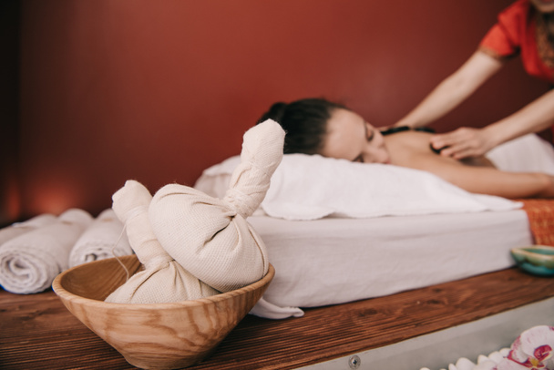   selective focus of herbal balls and asian masseur doing hot stone massage  - Photo, Image