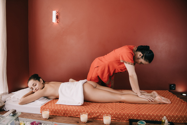vista lateral do massagista asiático fazendo massagem nos pés para mulher no salão de spa
  - Foto, Imagem