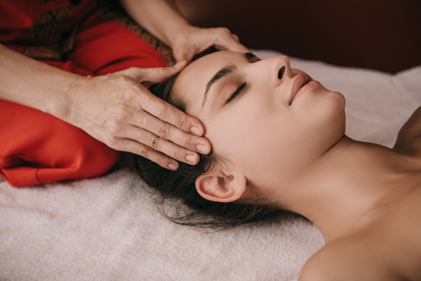 oříznutý pohled na masér dělá masáž tvář ženě v lázeňském salonu  - Fotografie, Obrázek
