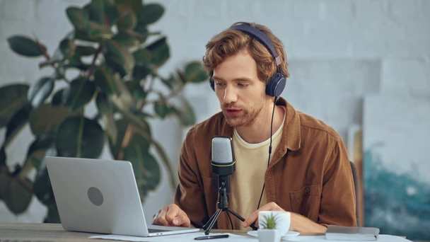 Muž, který poslouchá hudbu ve sluchátkách v mikrofonu při používání přenosného počítače - Záběry, video