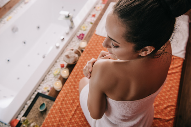High Angle view van aantrekkelijke vrouw met gesloten ogen in handdoek zittend op massage mat  - Foto, afbeelding