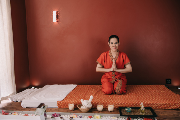 azjatycki masażysta w czerwonym stroju uśmiechnięty i pokazując ręce pozdrowienia  - Zdjęcie, obraz