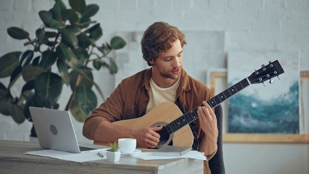 akustik gitar çalan ve dizüstü bilgisayarın yanında şarkı söyleyen adam - Video, Çekim