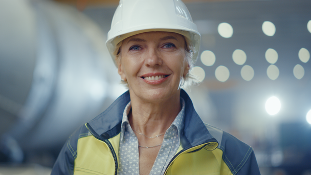 安全制服とハード帽子を身に着けているプロの重工業女性エンジニアの肖像,魅力的に笑顔.背景に溶接火花が飛ぶ集中していない大工業工場 - 映像、動画