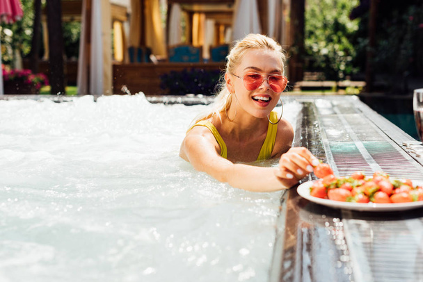 sexy smiling girl in swimsuit with strawberries in swimming pool - Valokuva, kuva