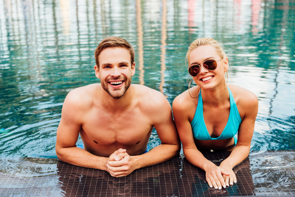 uśmiechnięta szczęśliwa para w basenie patrząc na kamerę - Zdjęcie, obraz