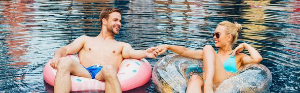 panoramiczny strzał uśmiechniętej pary trzymając ręce i patrząc na siebie w basenie - Zdjęcie, obraz