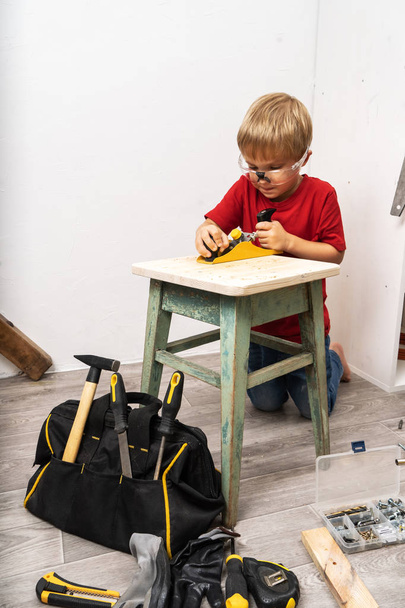 A little boy is planing an old stool with a planer. - Photo, Image