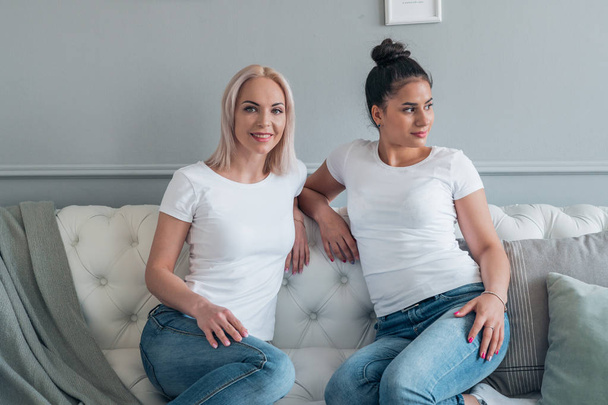 Two attractive girls dressed in casual style sitting on the couch in the room - Fotografie, Obrázek