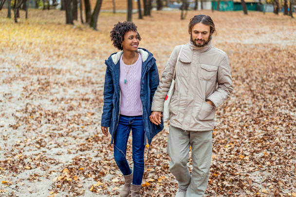 chico con un afroamericano chica en amor en otoño parque caminar al atardecer - Foto, imagen