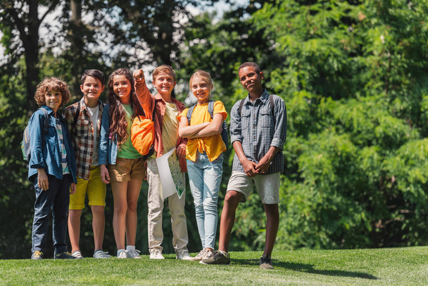 szczęśliwych wielokulturowych dzieci stojących na zielonej trawie  - Zdjęcie, obraz