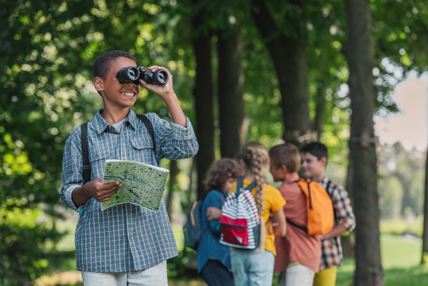 selective focus of happy african american kid looking through binoculars near friends  - Photo, Image