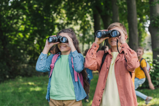 selective focus of happy kids looking through binoculars in park  - Foto, Imagen
