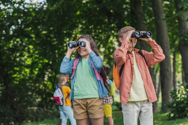 enfoque selectivo de niños alegres mirando a través de prismáticos en el parque
  - Foto, Imagen
