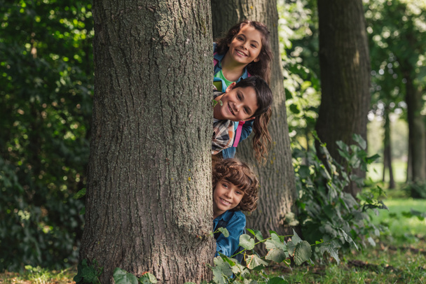 feliz chicos sonriendo cerca árbol tronco con adorable amigo
  - Foto, imagen