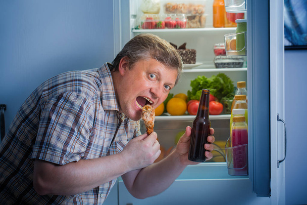 mature men at fridge  with beer and chicken's leg - Foto, Imagem