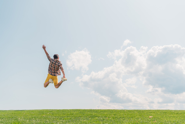 back view of boy with outstretched hand jumping against blue sky  - Fotografie, Obrázek