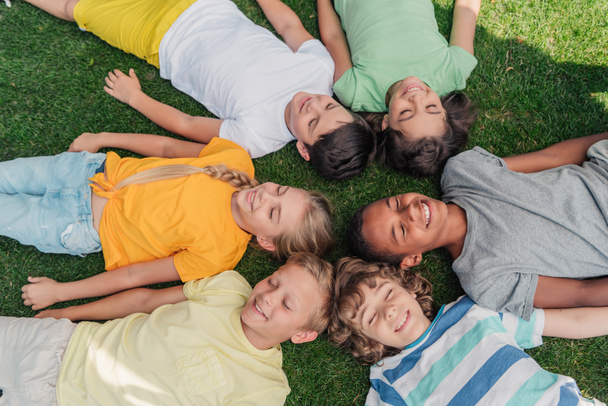 vue aérienne des enfants multiculturels heureux avec les yeux fermés couchés sur l'herbe
  - Photo, image