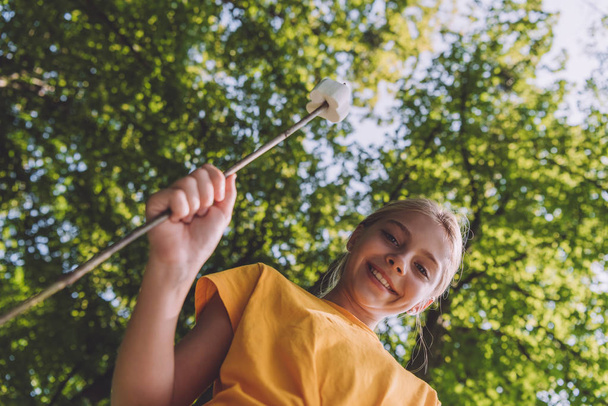 low angle view of happy kid holding sweet marshmallow on stick  - Fotó, kép