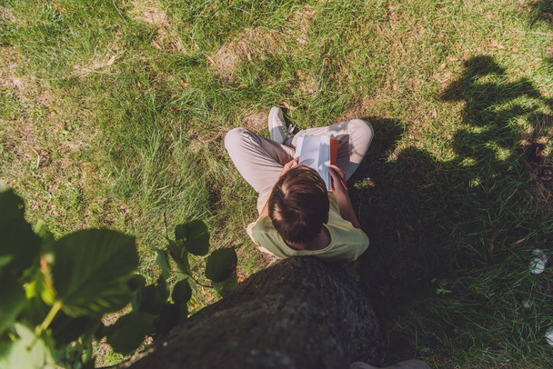 top view of boy holding notebook while sitting on grass   - Fotó, kép