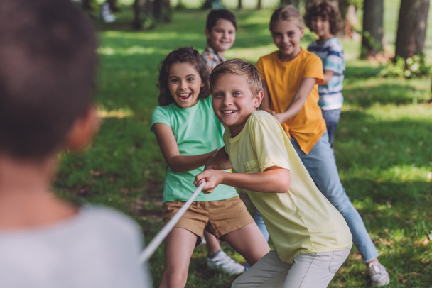 selective focus of cheerful kids competing in tug of war with african american boy  - Foto, Bild