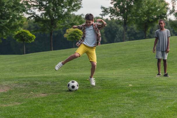rozkošný Afroameričan chlapec stojící na trávě u přítele, který hrál fotbal  - Fotografie, Obrázek