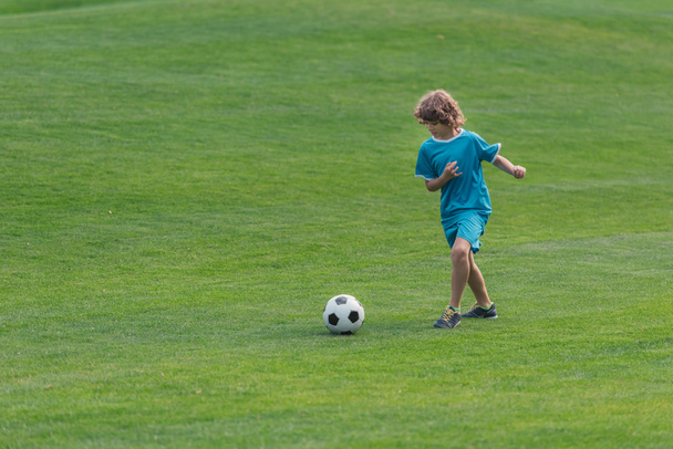 cute curly boy playing football on green grass  - Photo, Image