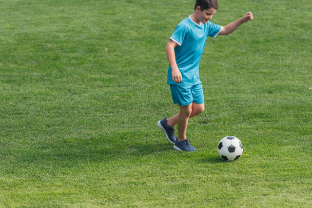 cute boy in sportswear playing football on green grass  - Фото, изображение