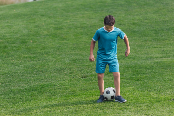 kid in sportswear standing on green grass with football  - Фото, зображення