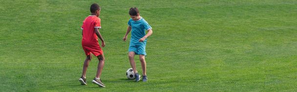 панорамный снимок милых мультикультурных детей, играющих в футбол на траве
  - Фото, изображение
