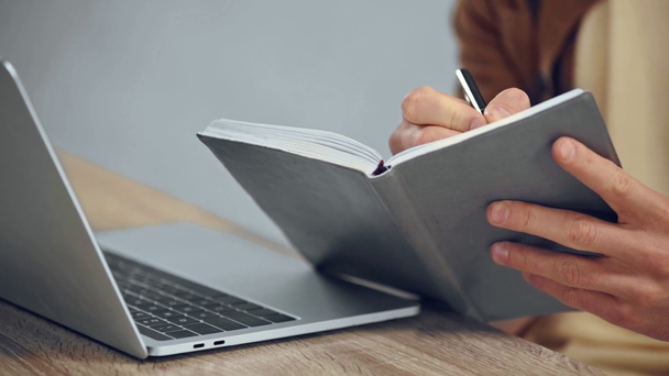 przycięte widok człowieka piśmie w notebooku i za pomocą laptopa - Materiał filmowy, wideo