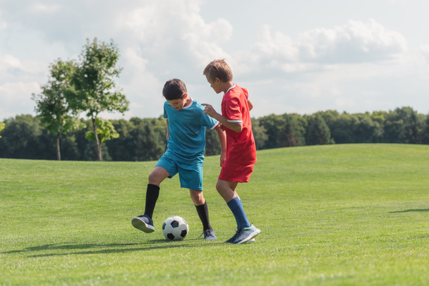 cute friends in sportswear playing football on green grass  - Foto, Imagem