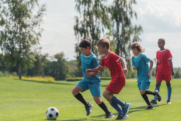 four multicultural kids playing football on grass   - Foto, Bild