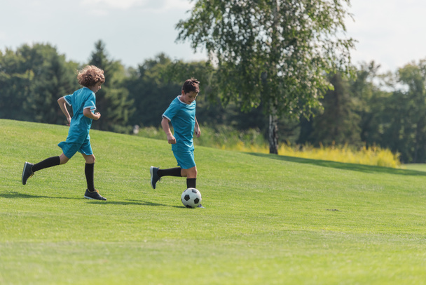 friends in blue sportswear playing football on green grass  - Фото, изображение