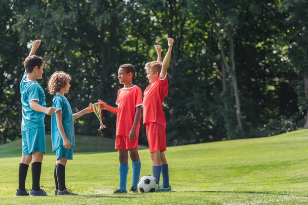 selective focus of cute multicultural kids gesturing near football  - Foto, afbeelding