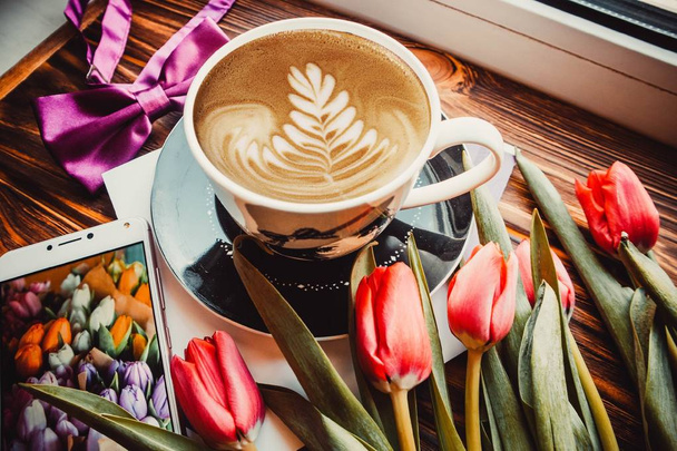 Kuppi kahvia, puhelin ja kukkia puinen ruskea tausta - Valokuva, kuva