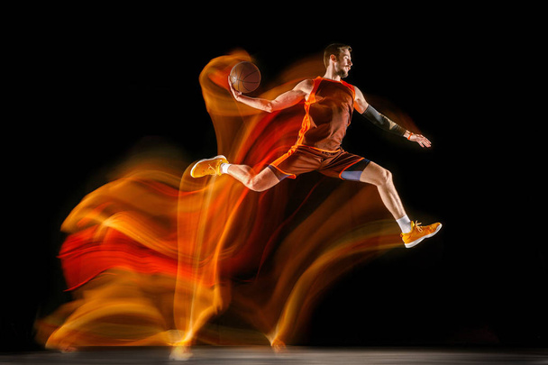 Young caucasian basketball player against dark background in mixed light - Fotografie, Obrázek