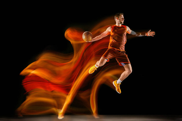 Mladý Kavkazský basketbalista proti tmavému pozadí ve smíšeném světle - Fotografie, Obrázek